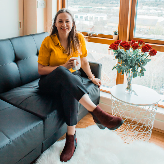 Mergina sėdi ant juodos sofos, rankoje laiko puodelį su kava